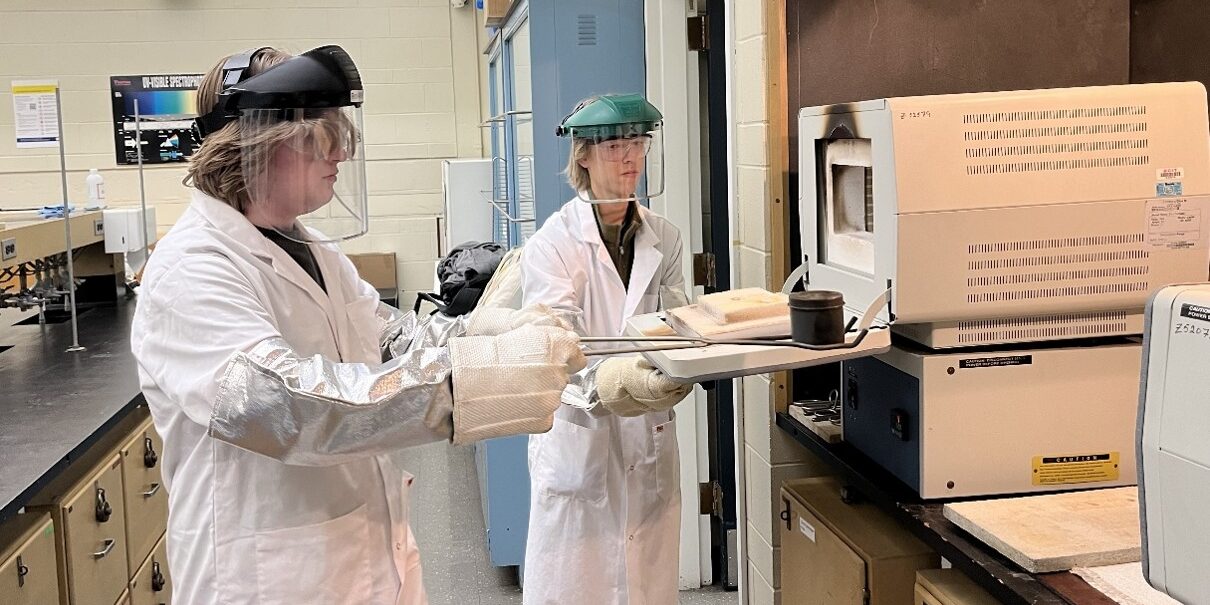 Two students working in a lab with protective gear.