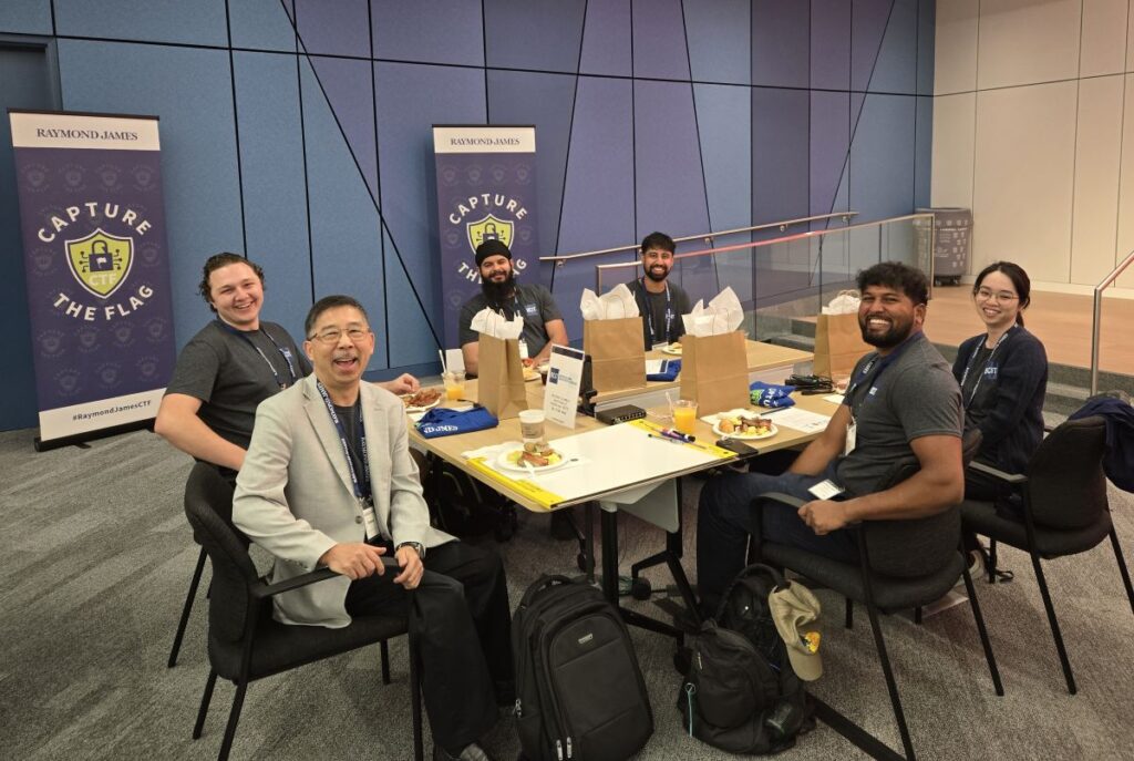 five smiling students and instructor sit at a table with laptops